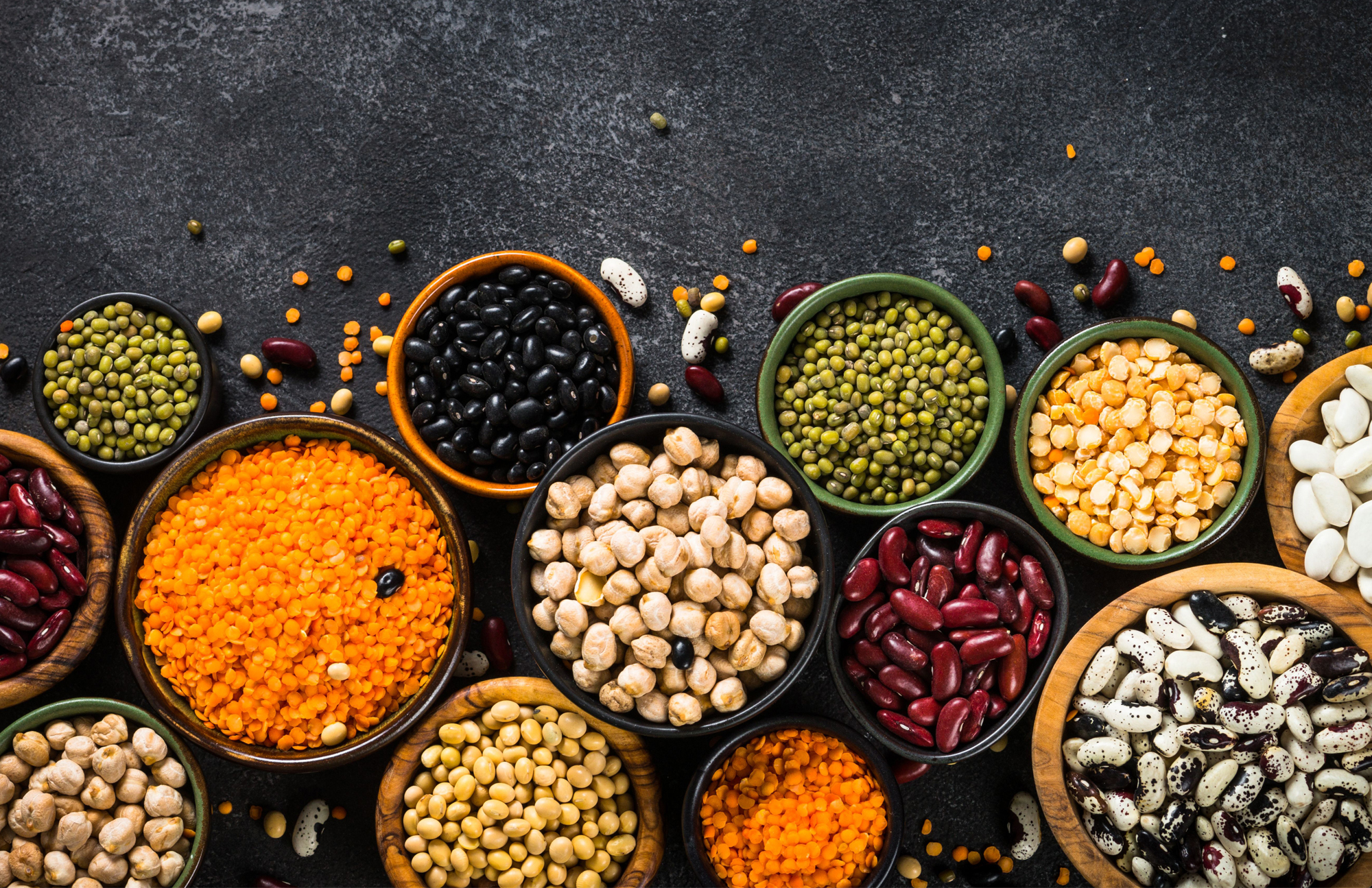 A variety of beans: Kidney, garbonzo, pinto, chick pea, peas, black beans all in containers in a photo looking down on them