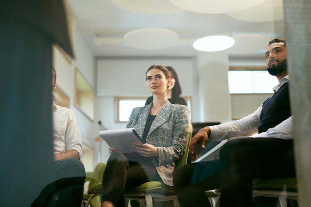 a woman and a man sitting and listening to a lecture in an office. 