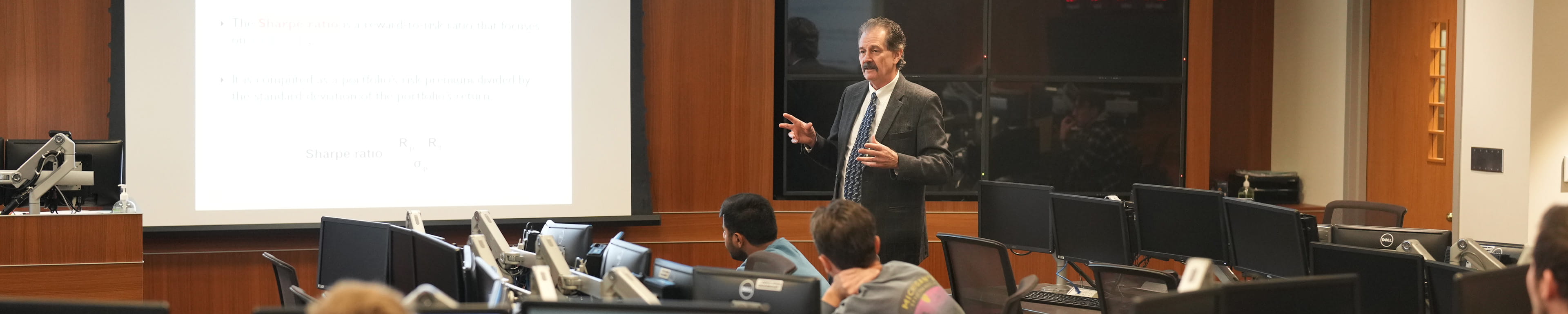 An image of a professor teaching his class with multiple kinds of media.
