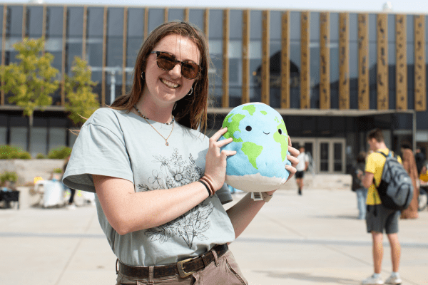 Smiling student wearing sunglasses and holding a stuffed animal globe