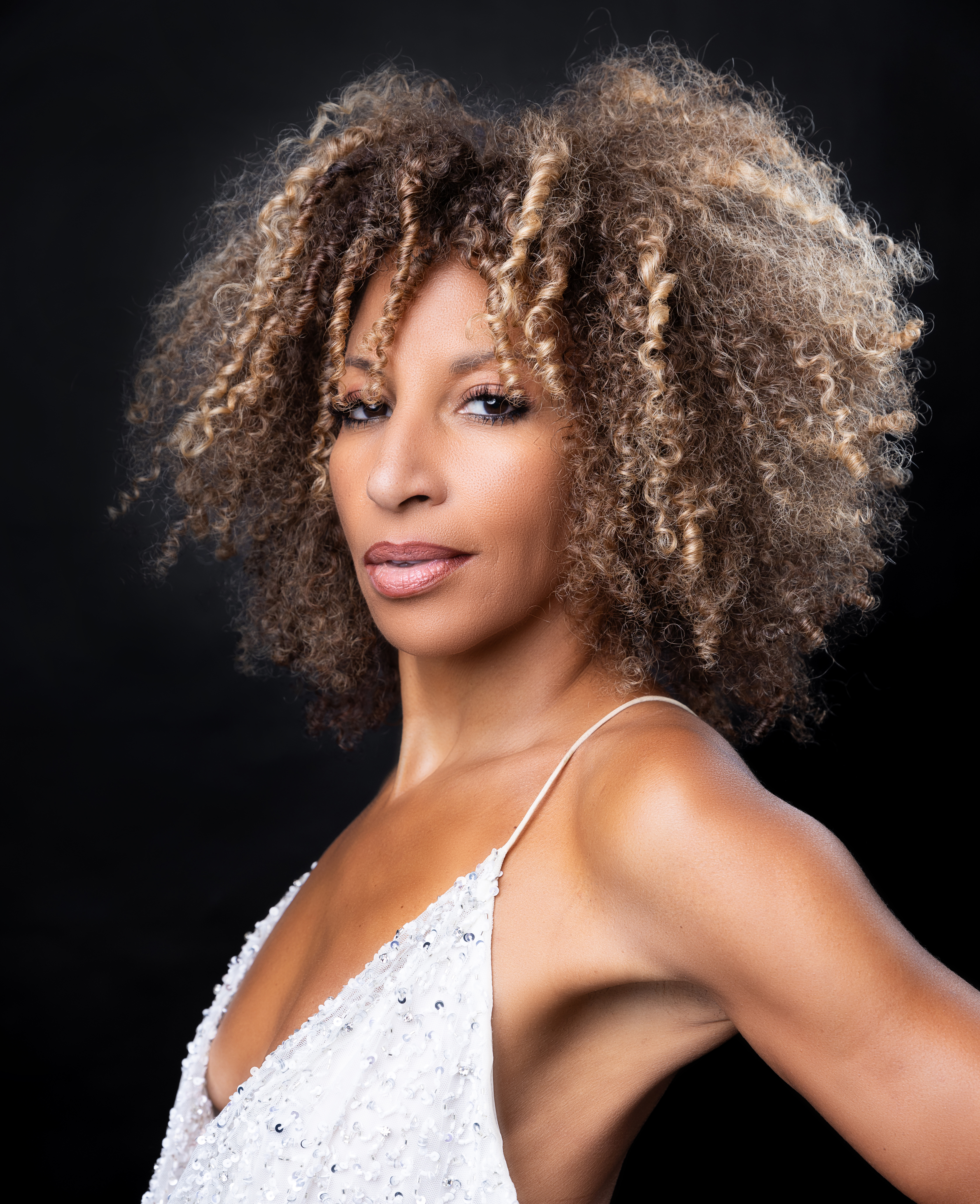 A light-skinned woman with curly hair wearing a sleeveless white top.