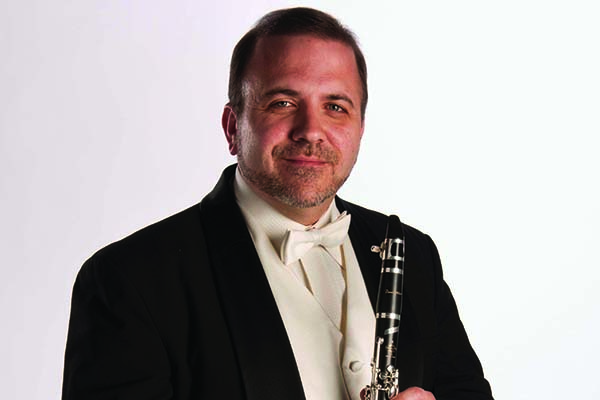 Smiling man in a tuxedo holding a clarinet.