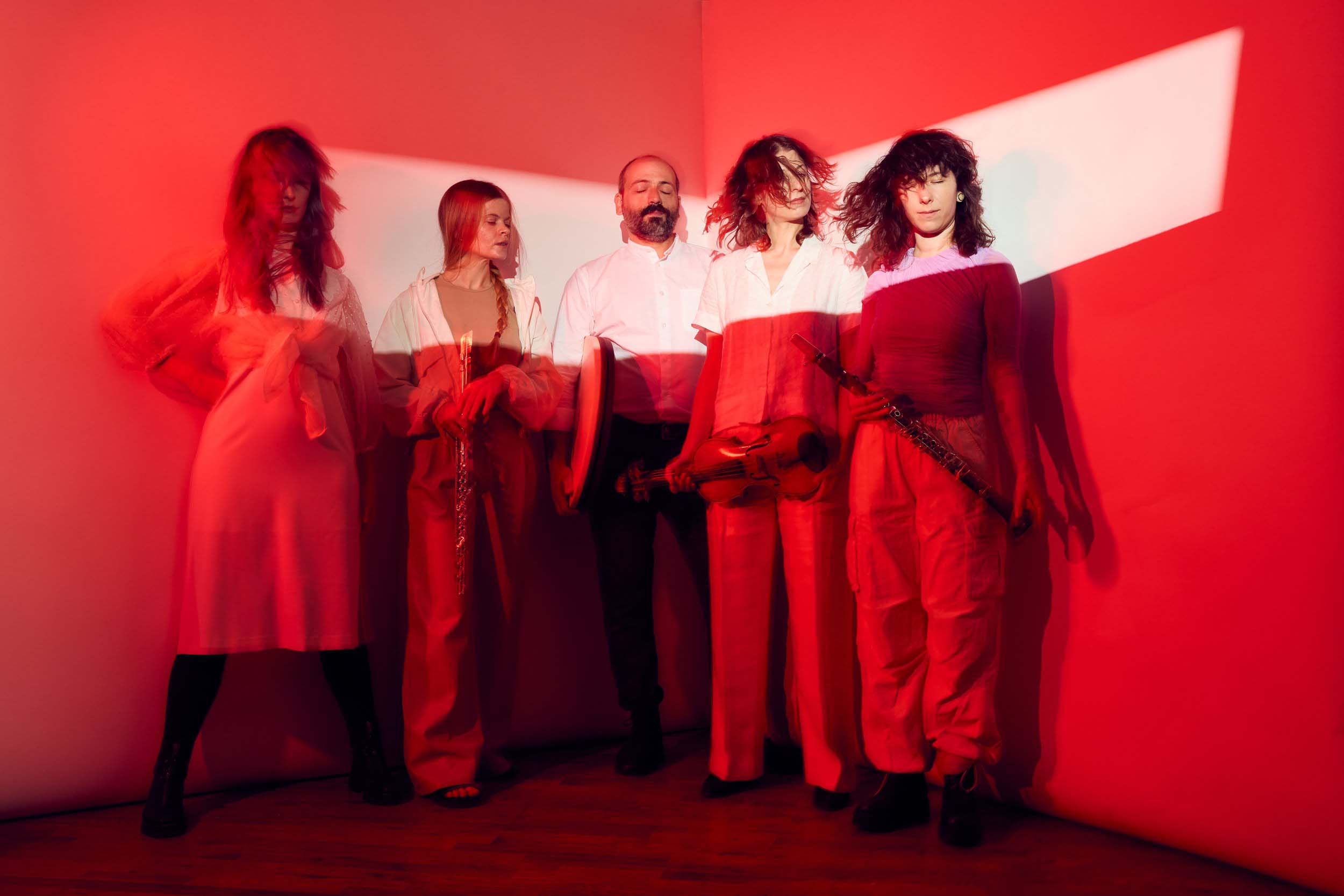 Five musicians holding instruments, standing in a line under a red light.