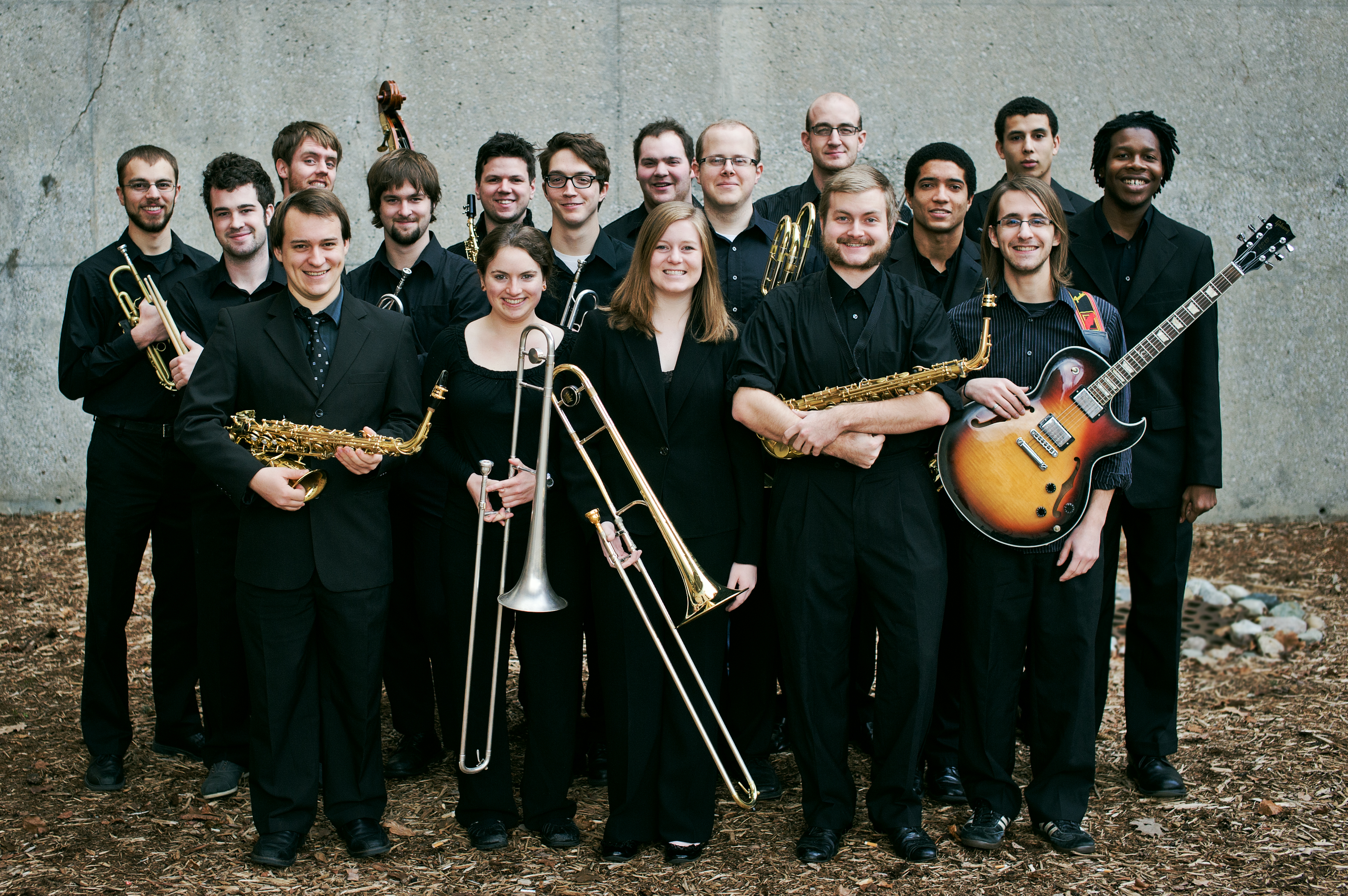 Seventeen smiling musicians holding instruments, standing in a group.