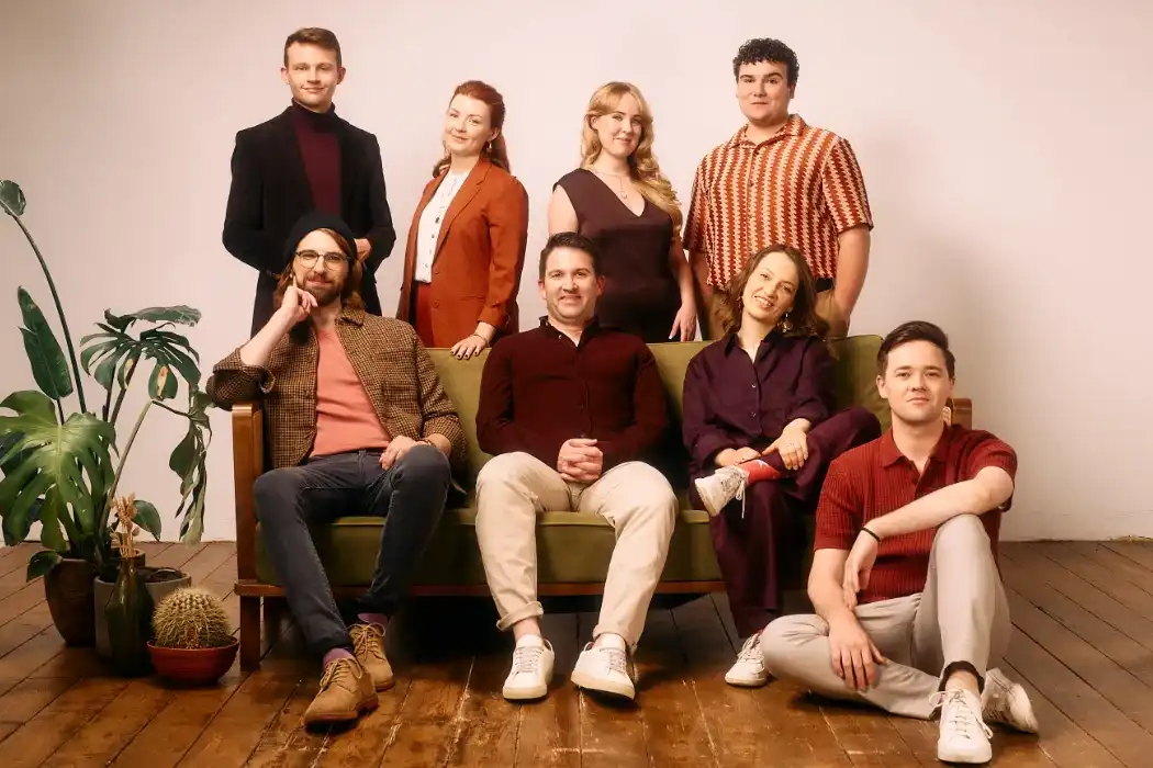 Group of vocalists sitting on couch. Collection of plants to their right.