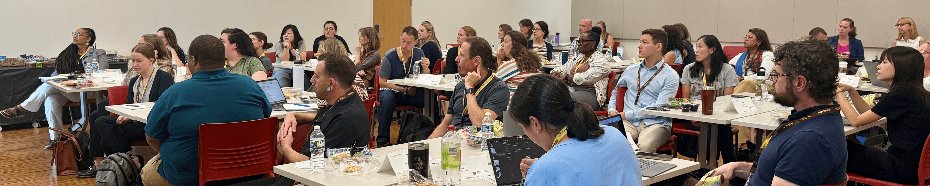 A large group of new faculty at orientation, sitting at tables and listening to a presentation