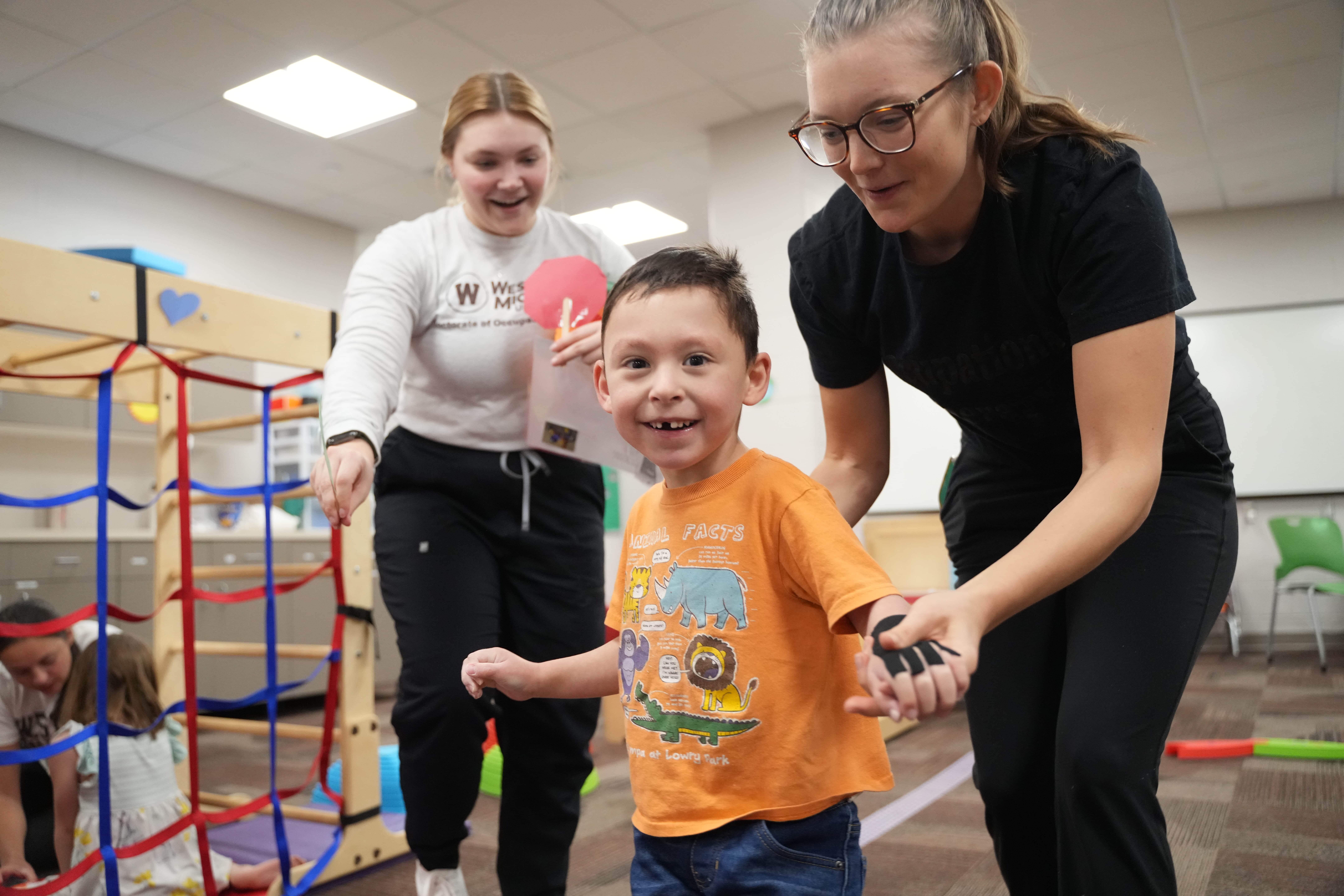 Two female WMU OT students help a young boy in the pediatric clinic