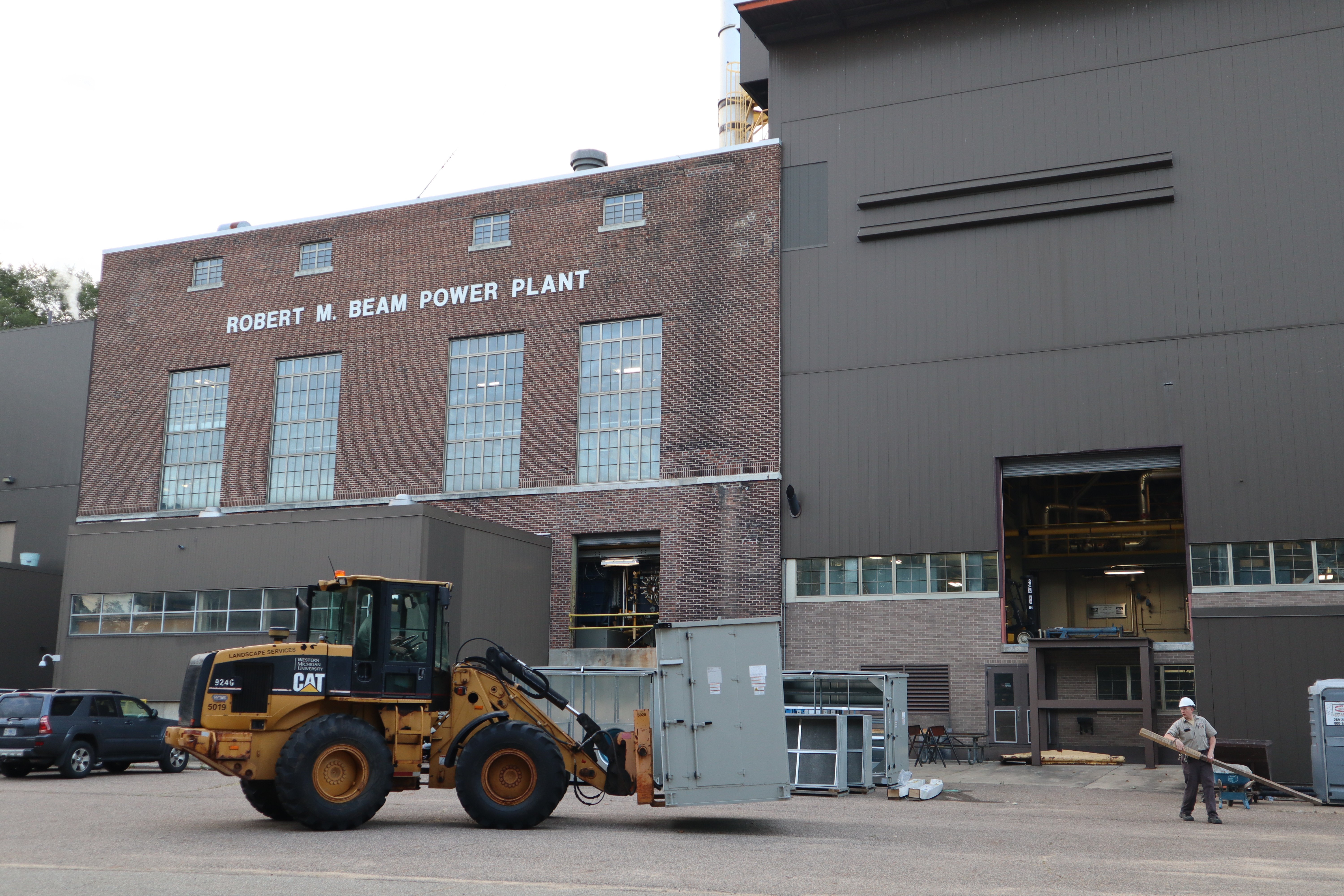 Equipment is getting hauled across a lot in front of the Beam Power Plant.
