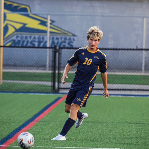 Soccer player in a blue uniform running with ball to net.