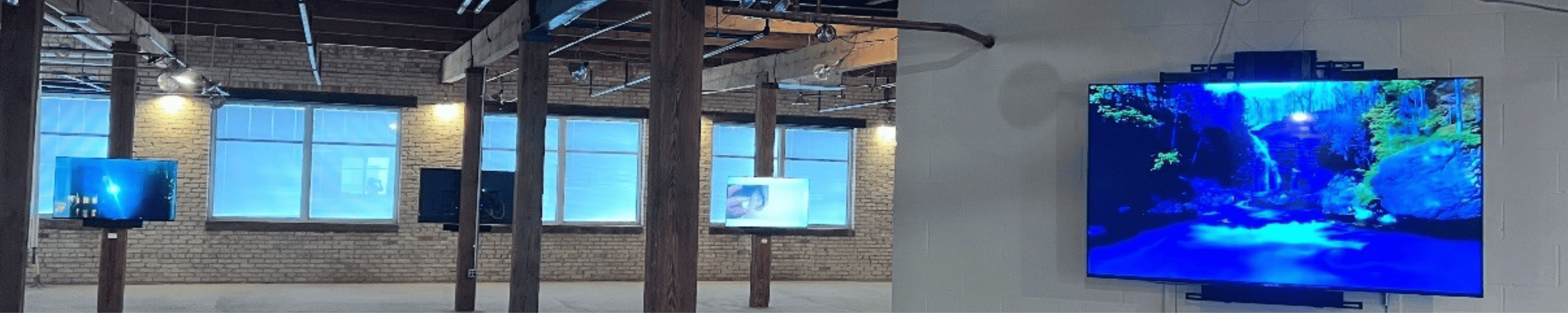 A photo of the industrial, loft-like fifth floor Resonant Gallery space, with TV monitors on display throughout