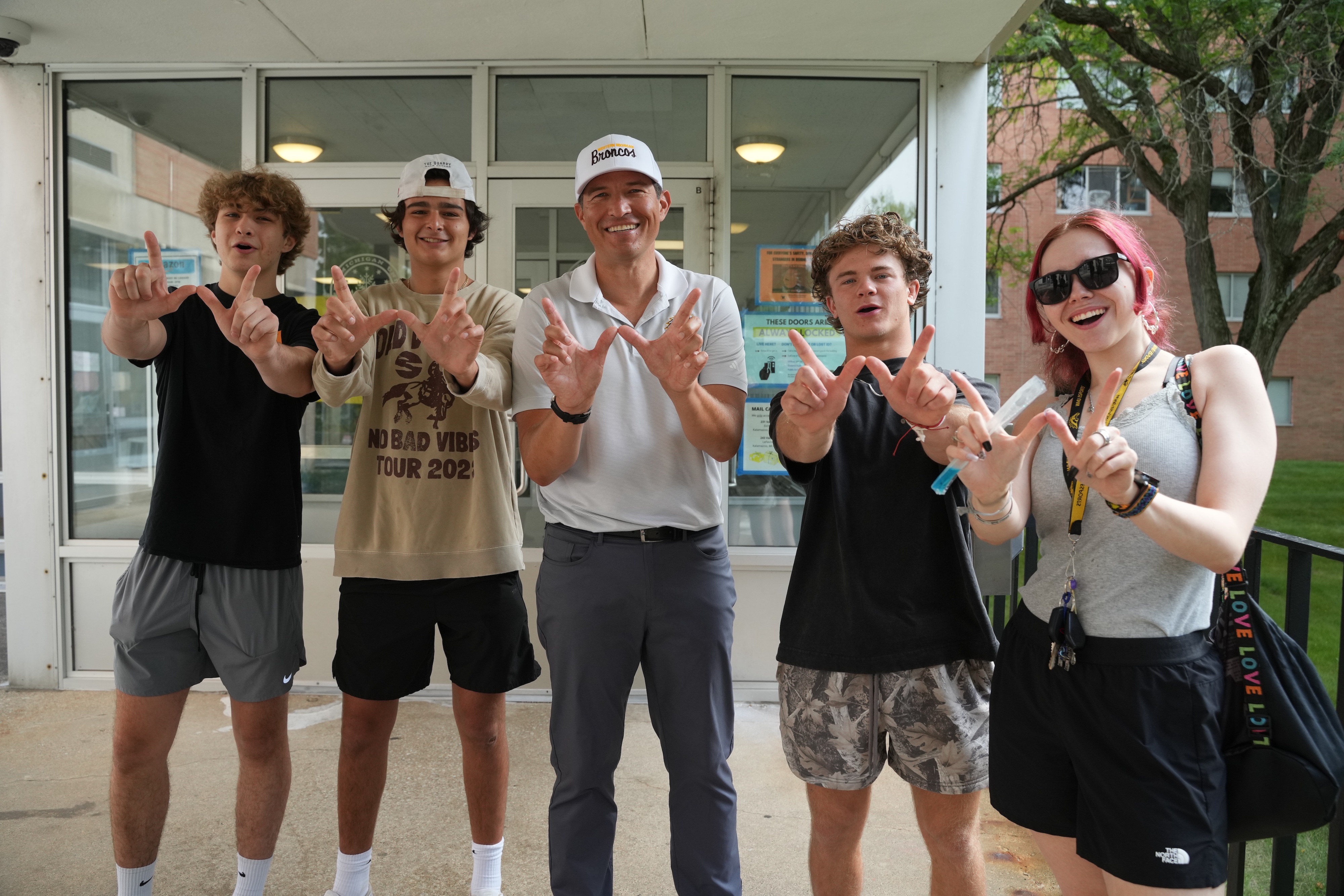 President Kavalhuna holds up a W with several students.