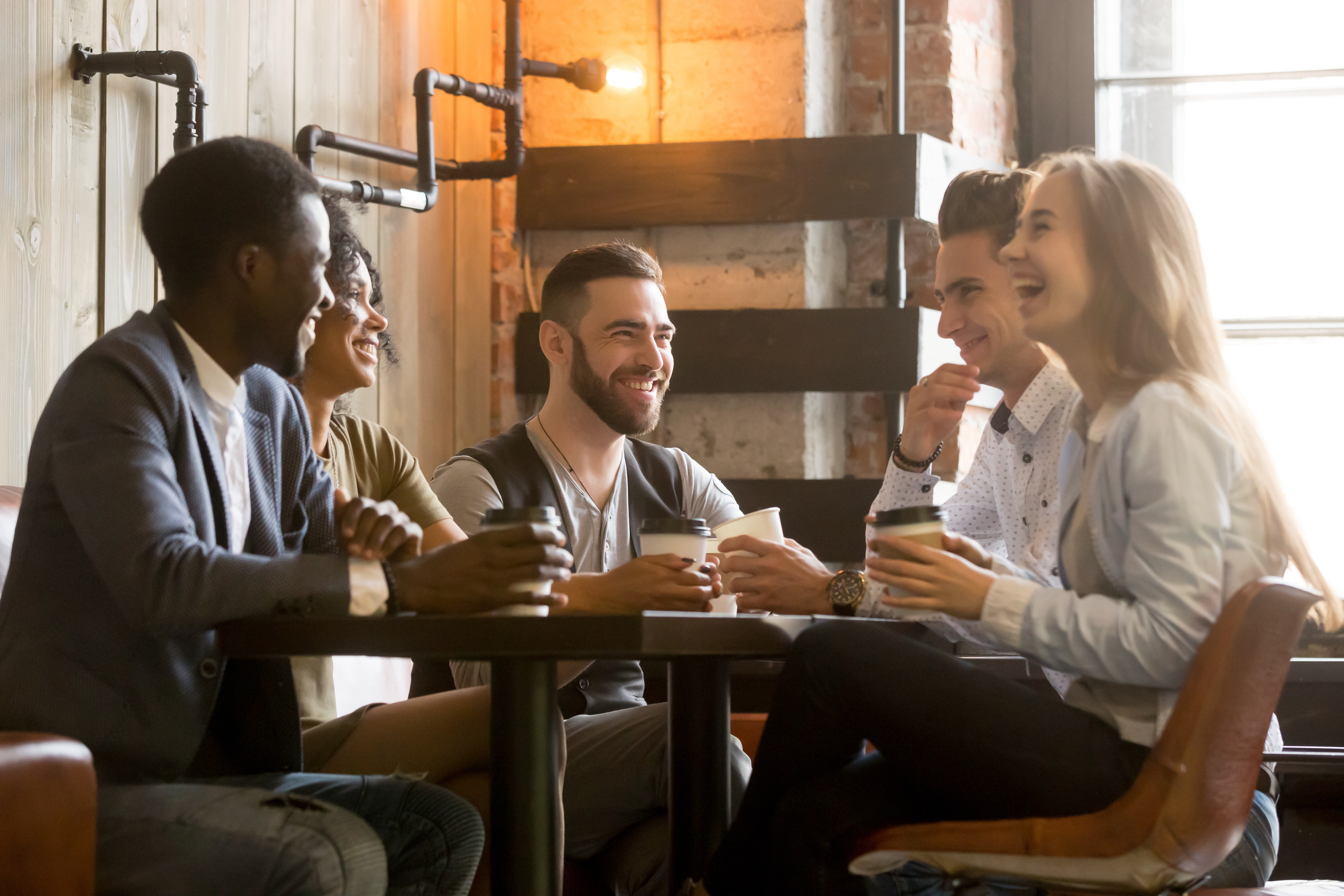Diverse group of people sitting at a table in a coffeeshop talking and drinking coffee. A lot of deep colors in this image.
