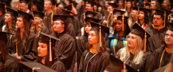 A group of WMU students at graduation listening to a speech.