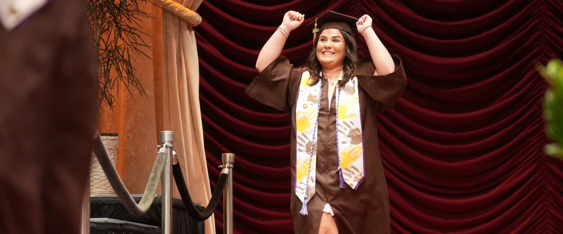 Female social work graduate walks across the stage smiling with hands in the air.