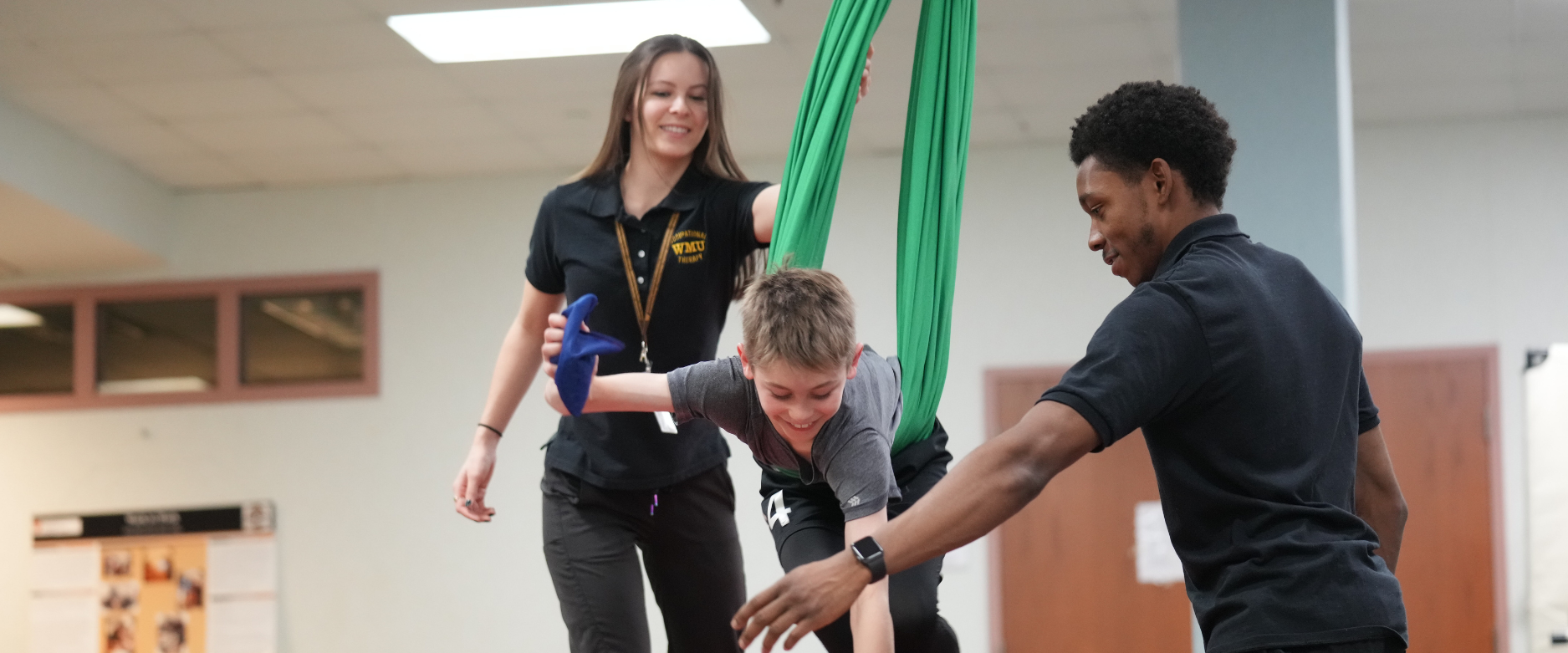 Male and female occupational therapy students interact with a small child on a swing