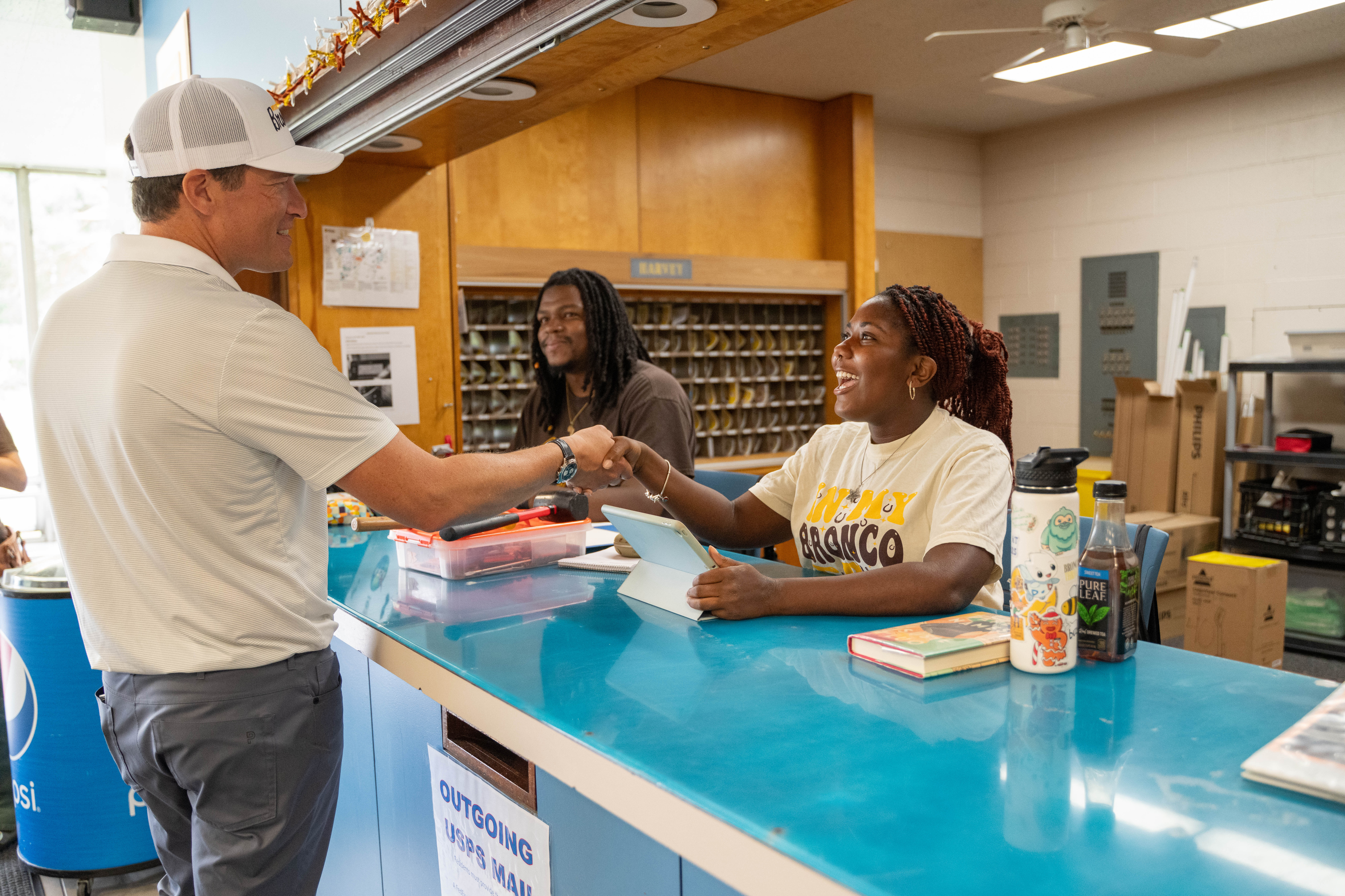 Two student employees at the residence hall front desk shake hands with WMU's president on move-in day.