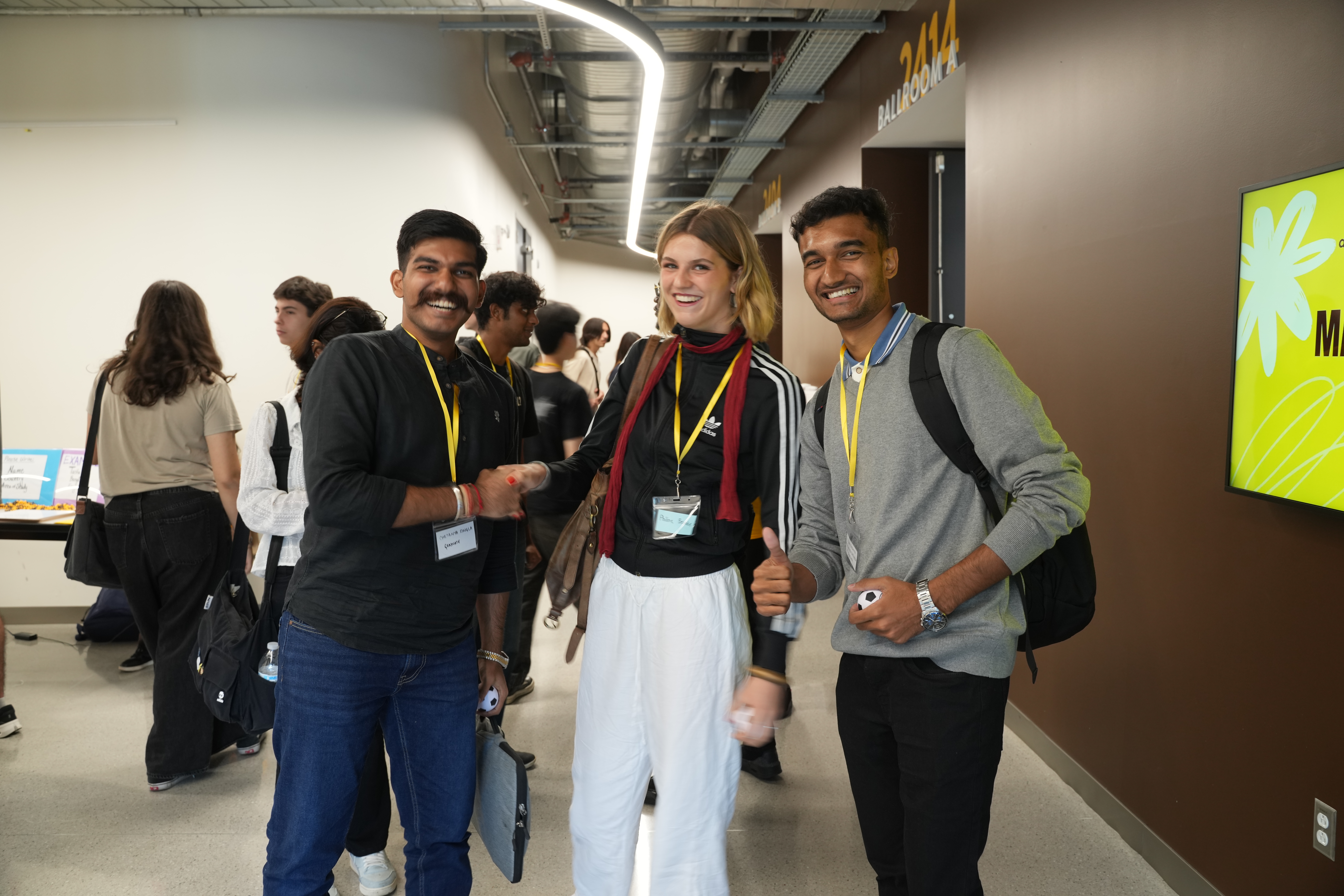 Three WMU international students smile for a picture at international student orientation in the WMU Student Center. More international students converse and browse behind them.