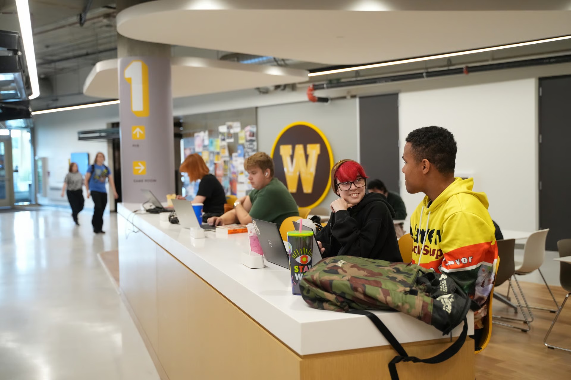 Students sit at a counter with their laptops and backpacks outside Refresh Market.