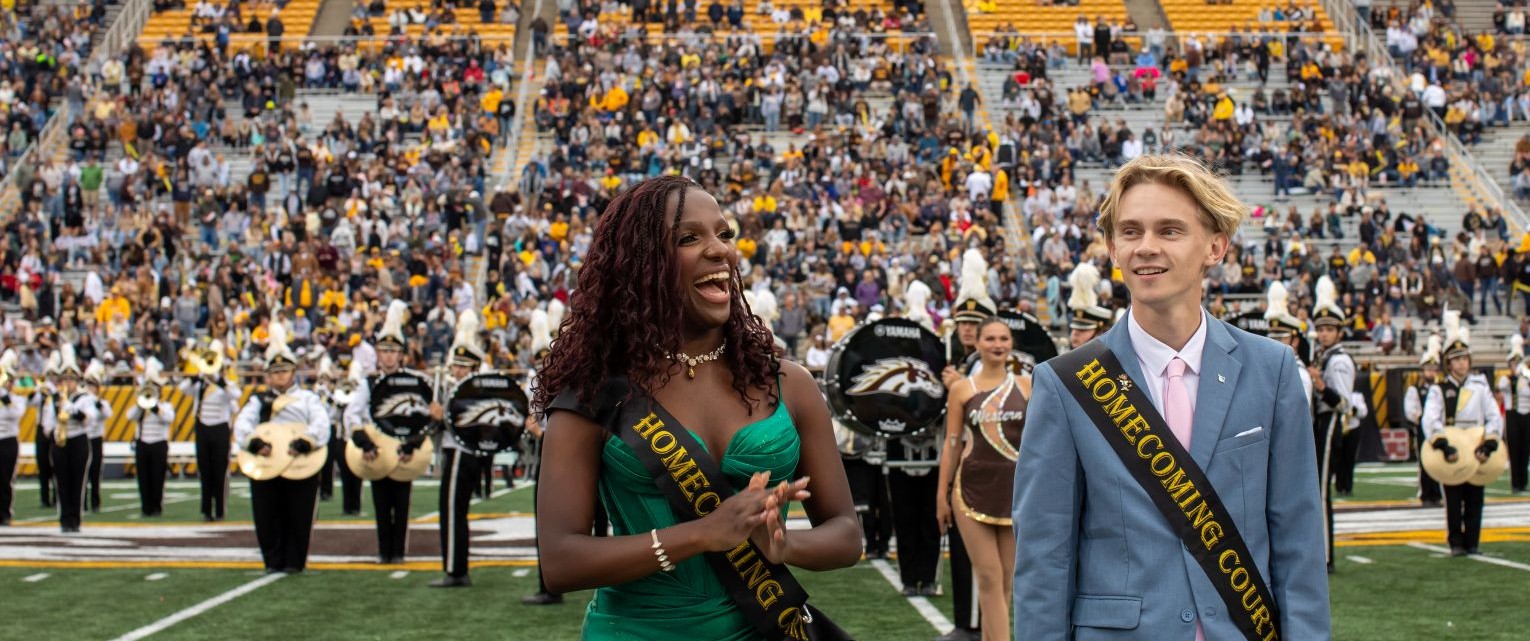 Members of the Western Michigan University Homecoming Court are recognized on the football field during Homecoming festivities with the marching band and spectators in attendance.