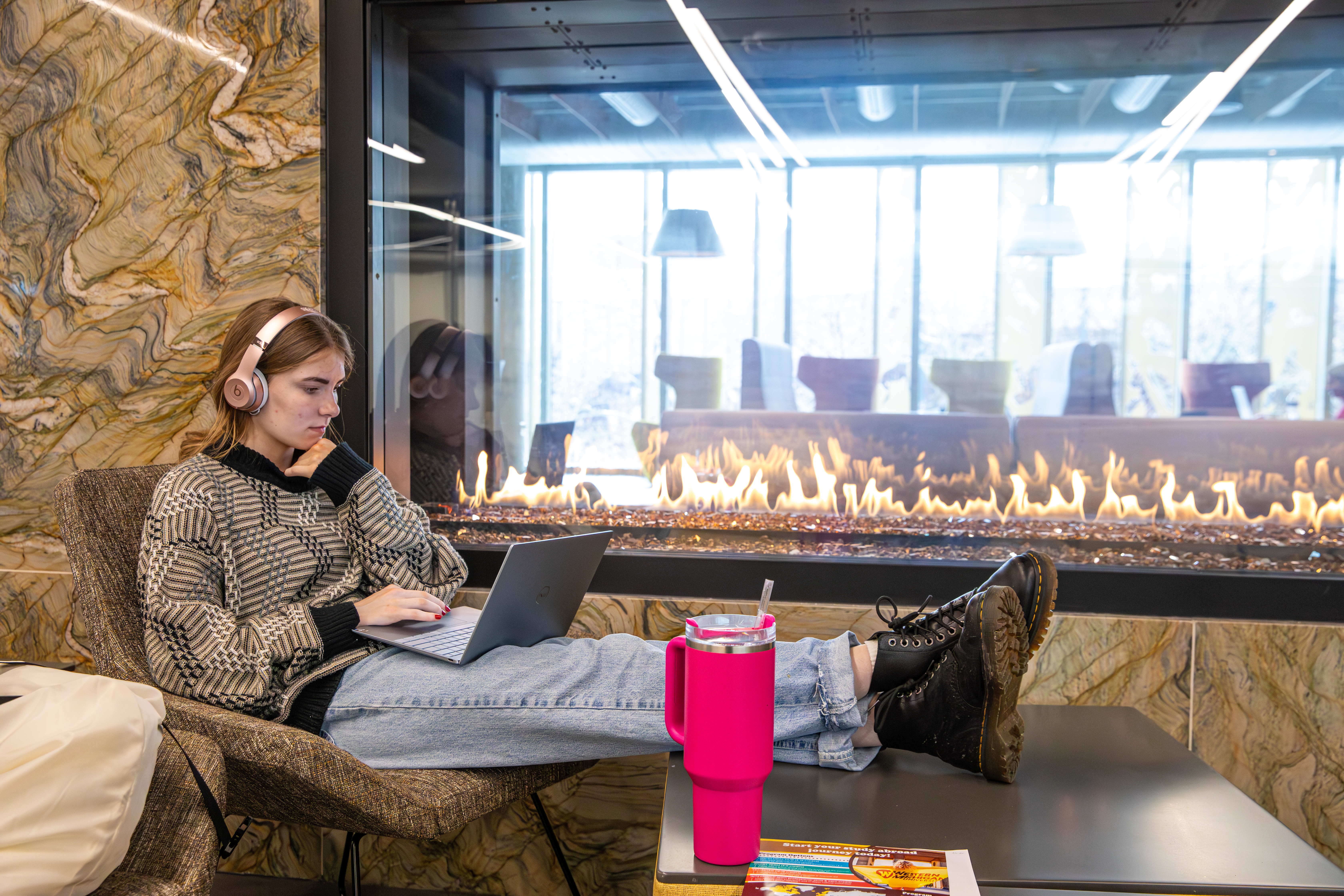 Student working on laptop sits by fireplace at the Student Center