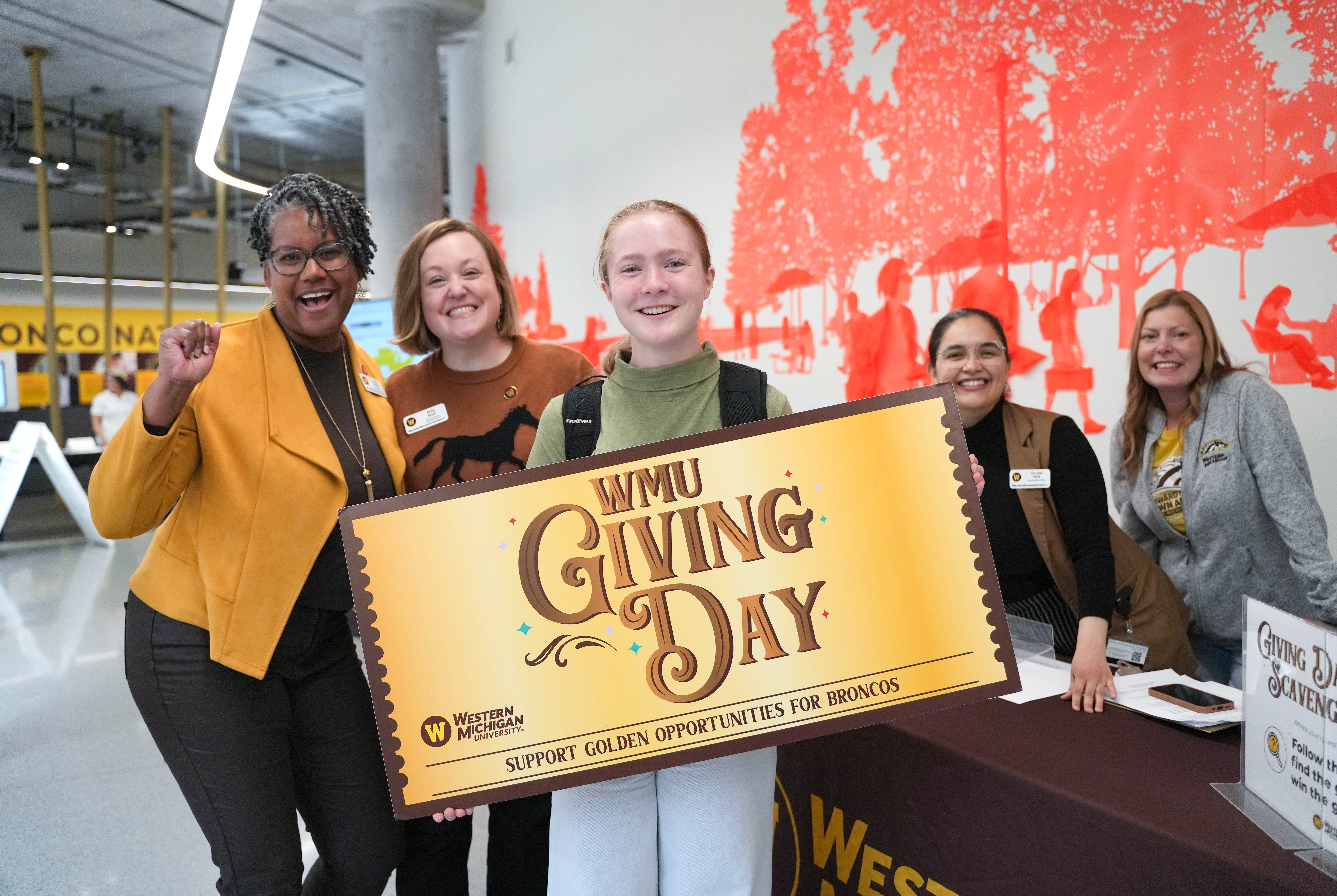 A group of people stand around a student holding a large "WMU Giving Day" golden ticket.