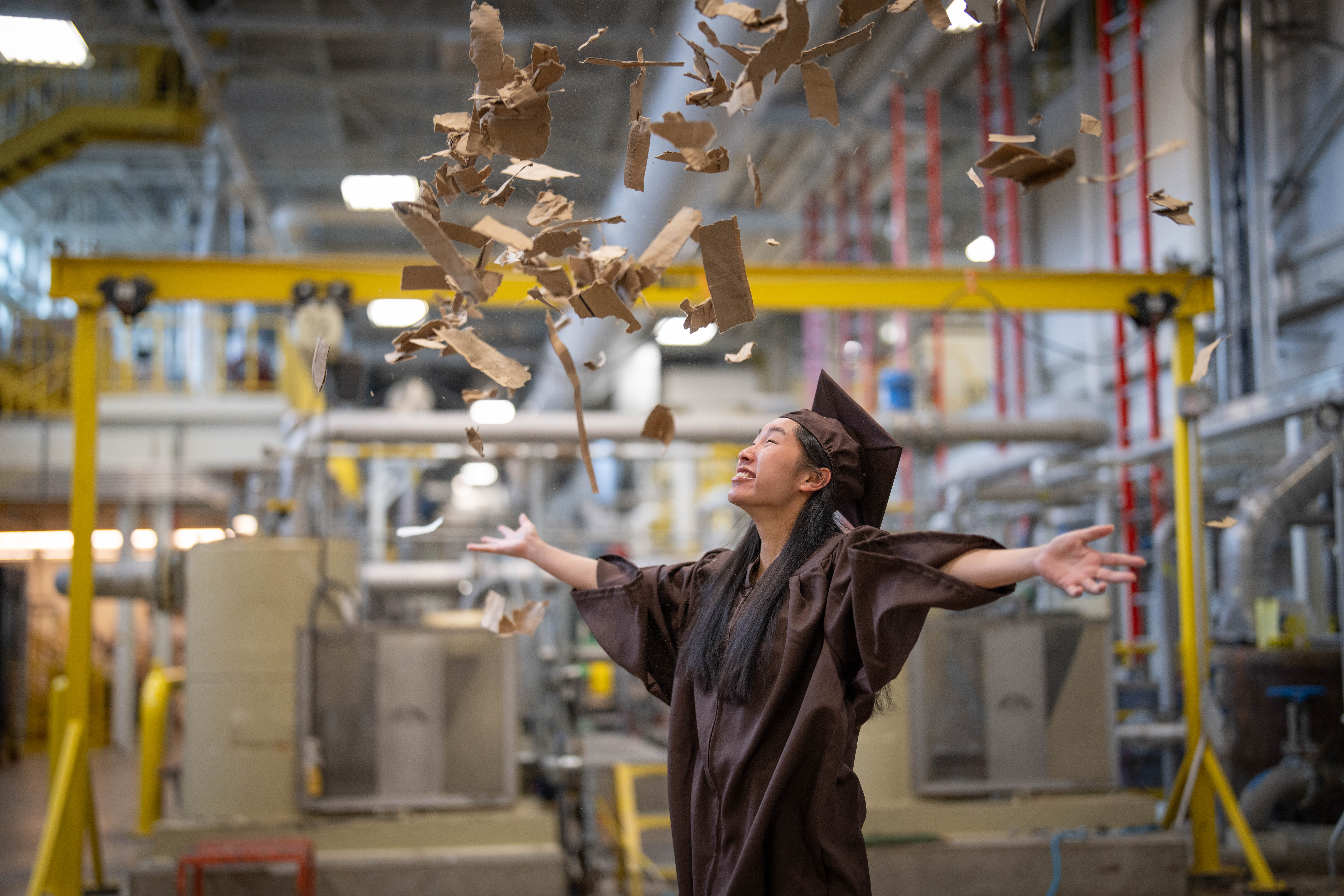 An undergraduate in the Paper Pilot Plant in their graduation regalia. 