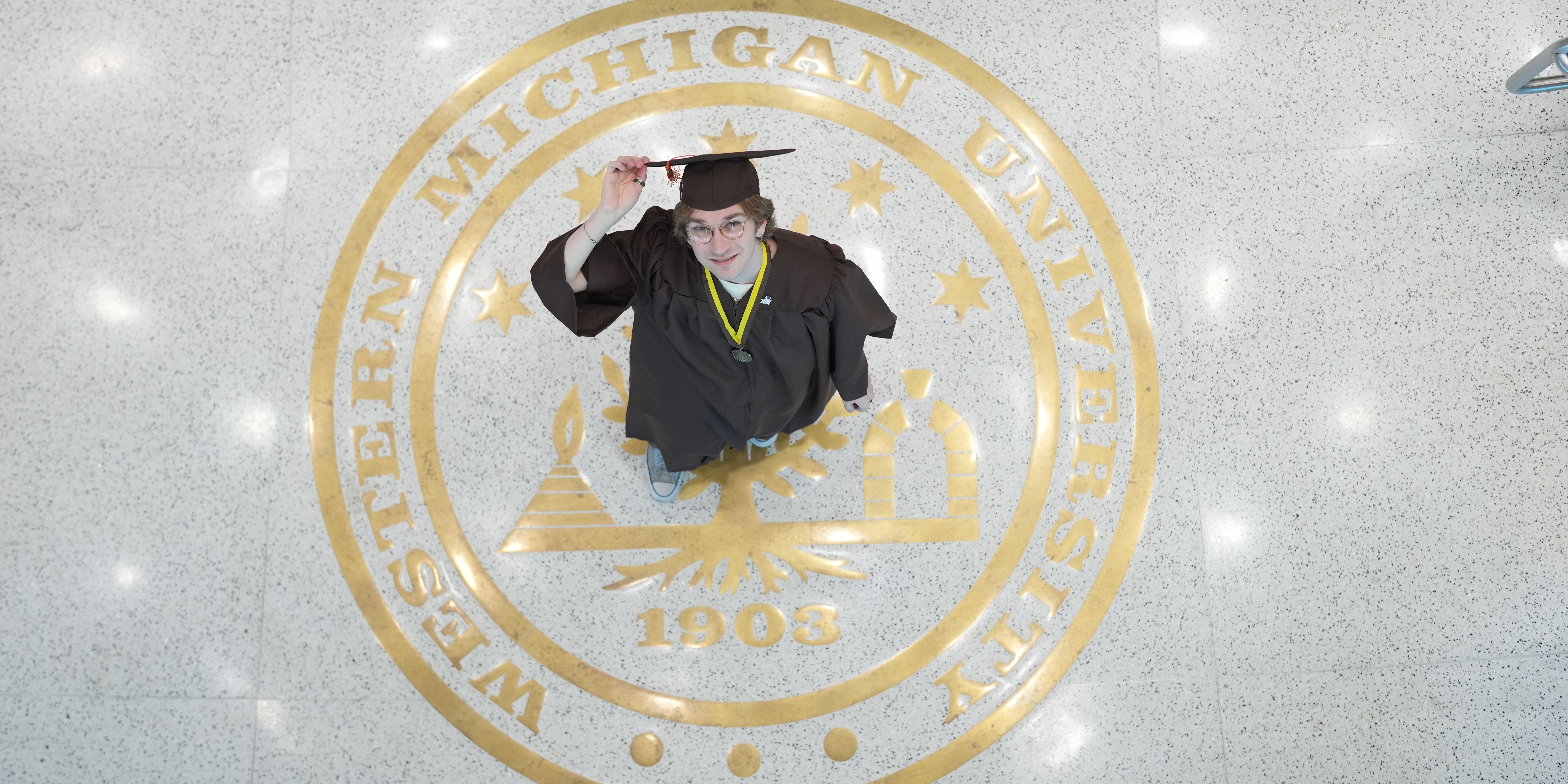A student standing on the crest of WMU, looking up at the camera. 