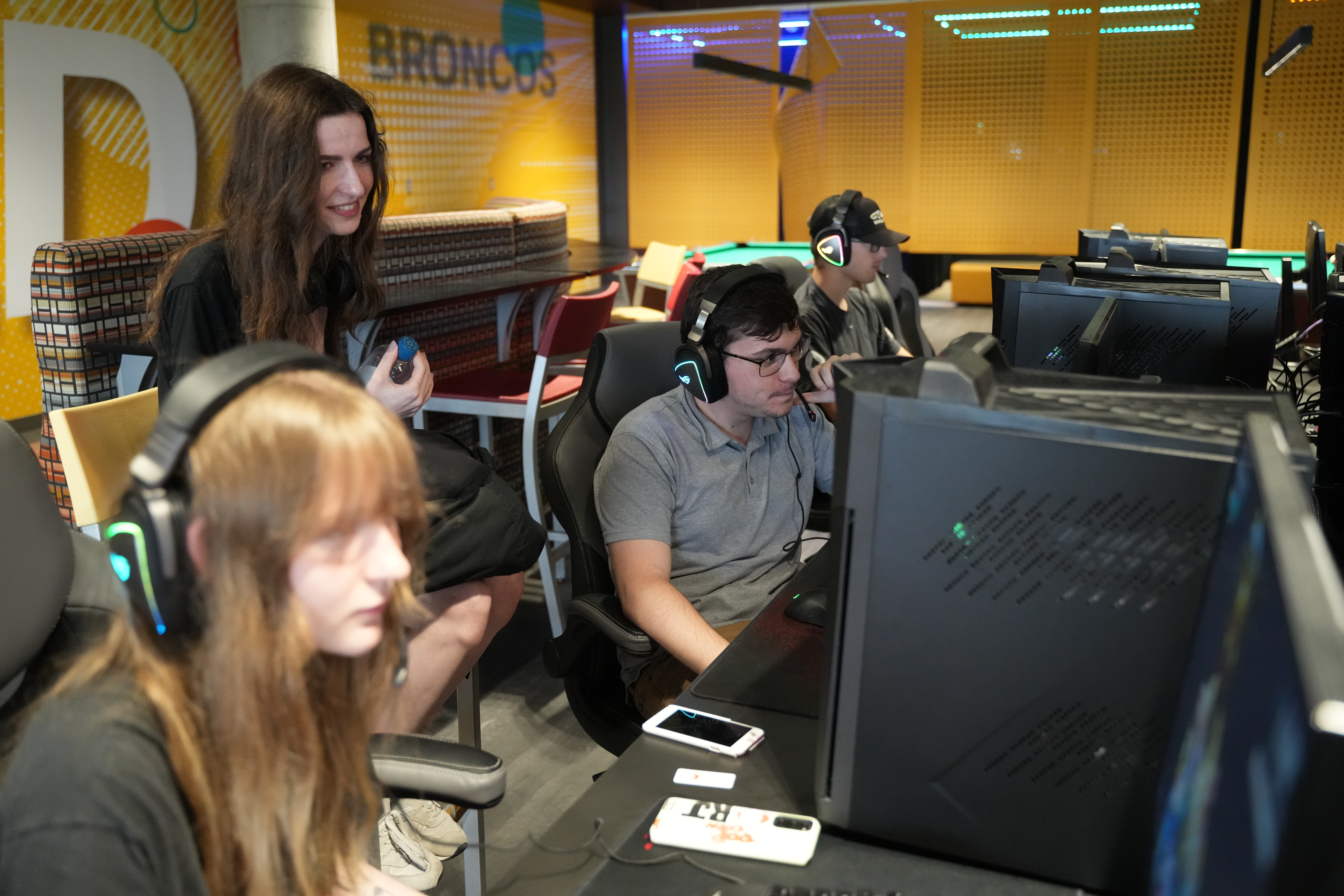 Several students wearing headsets play Esports games at a bank of computers in the Game Room.