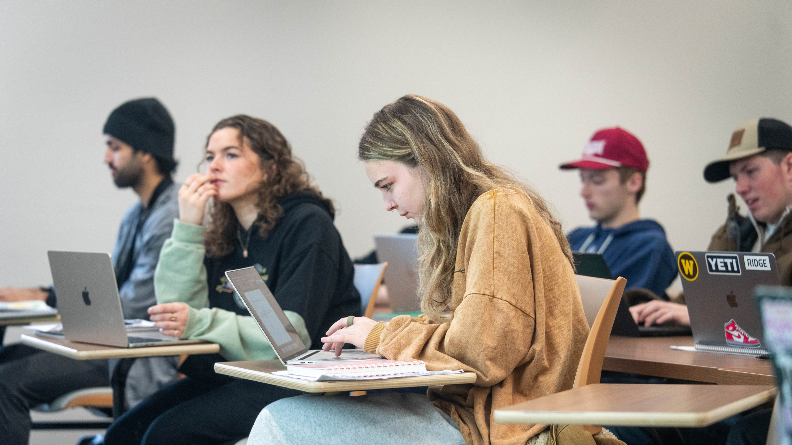 Students sit in a classroom, taking notes, looking quizzically forward. 