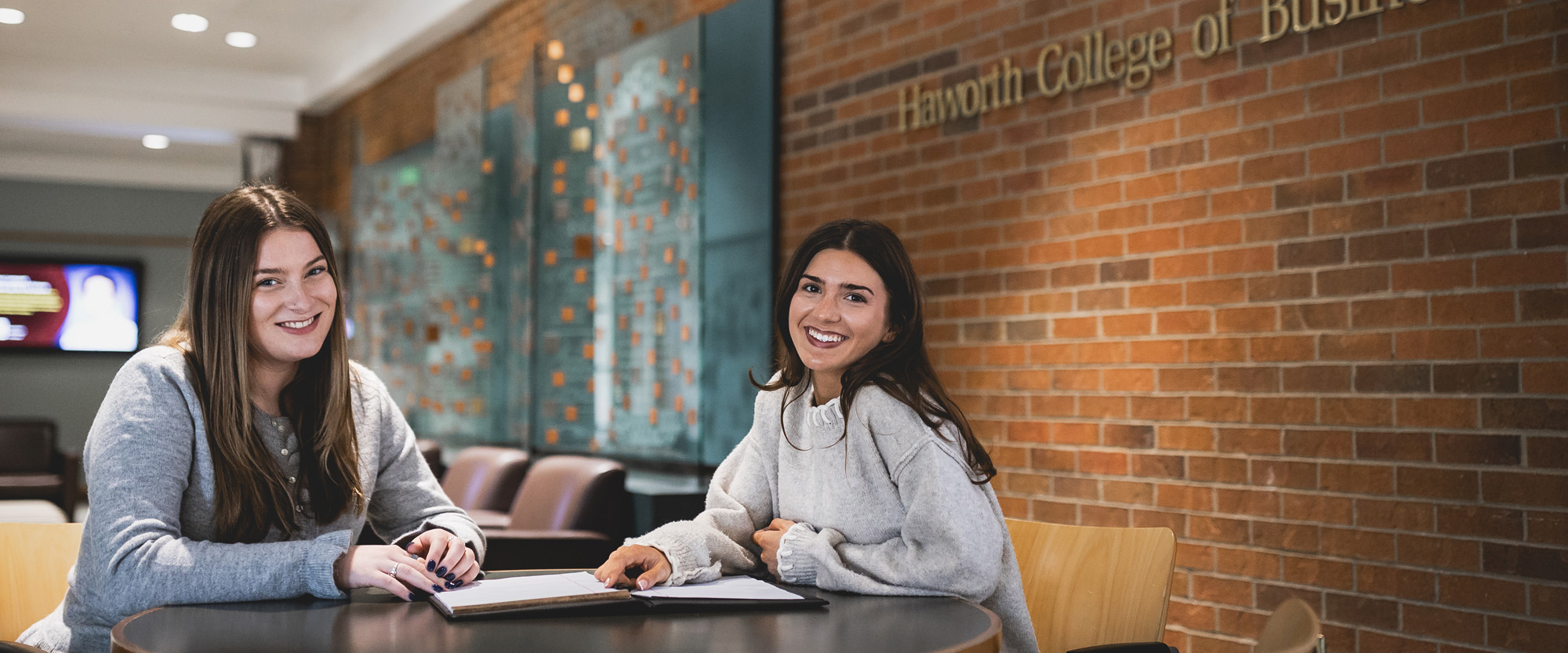 Two marketing students at a table in Schneider Hall lobby