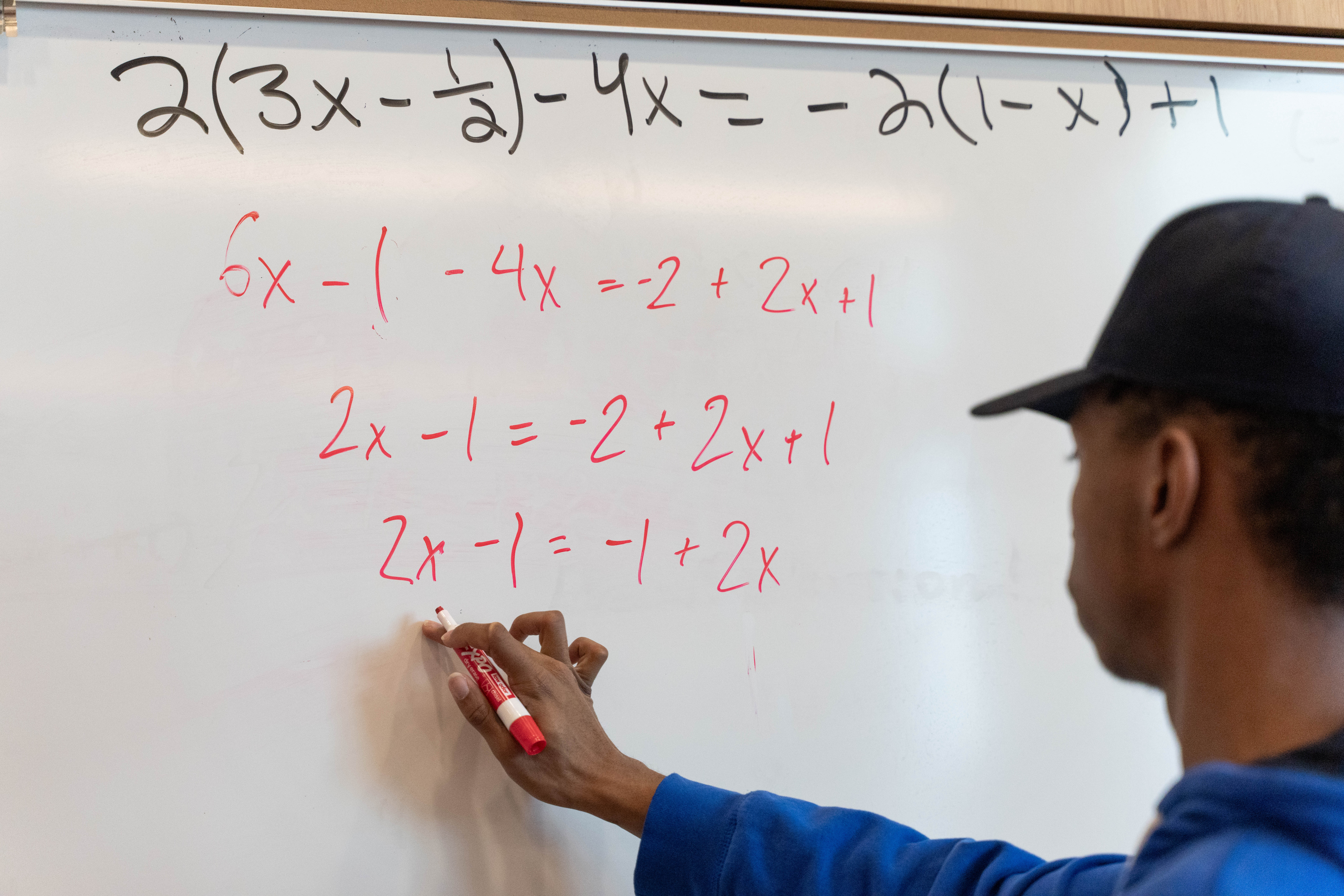 student writing algebra problem on a white board.
