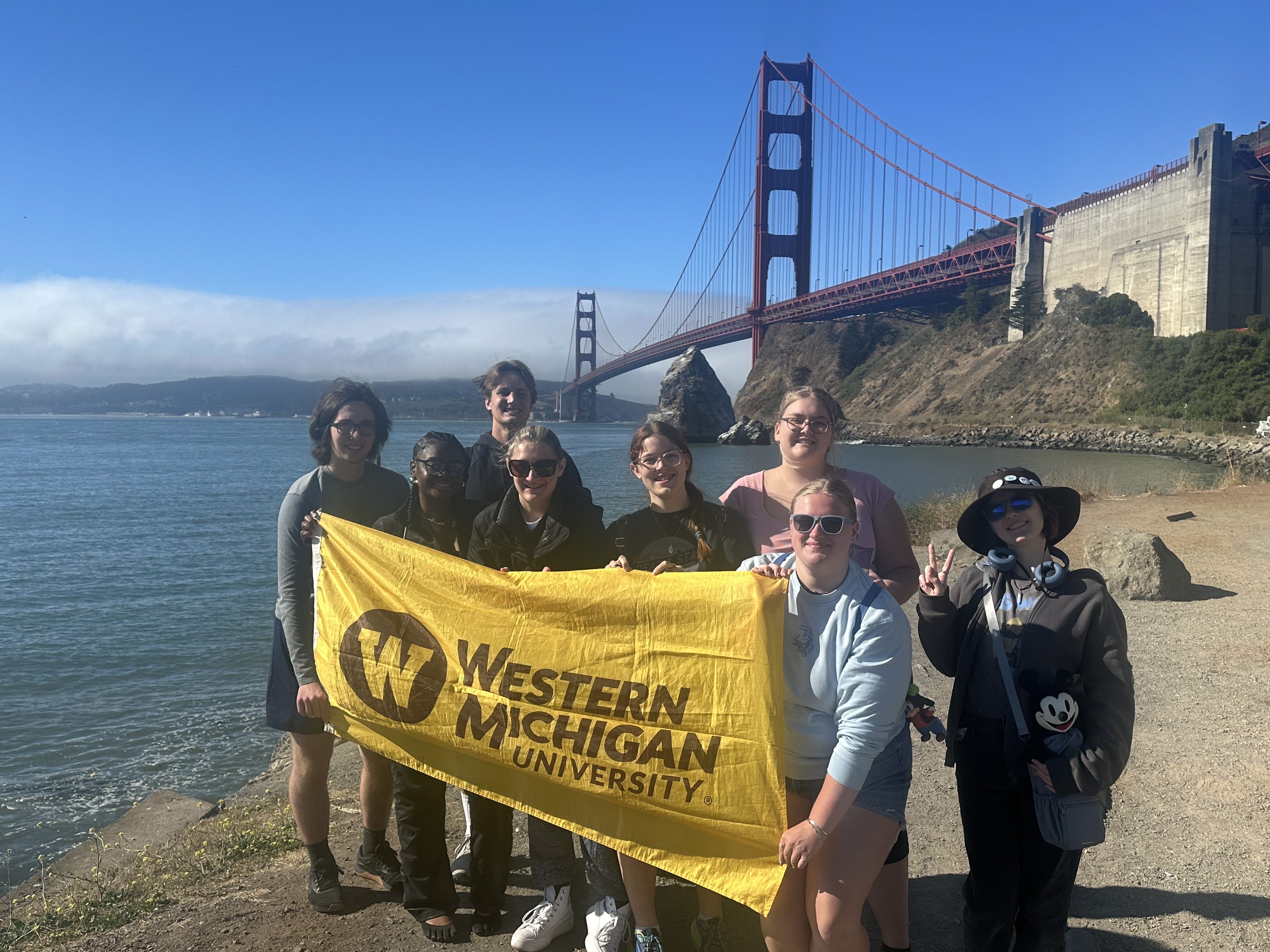 Students traveling with the SIS Walt's Pilgrimage course stand in front of the Golden Gate Bridge in San Francisco holding a WMU flag. 