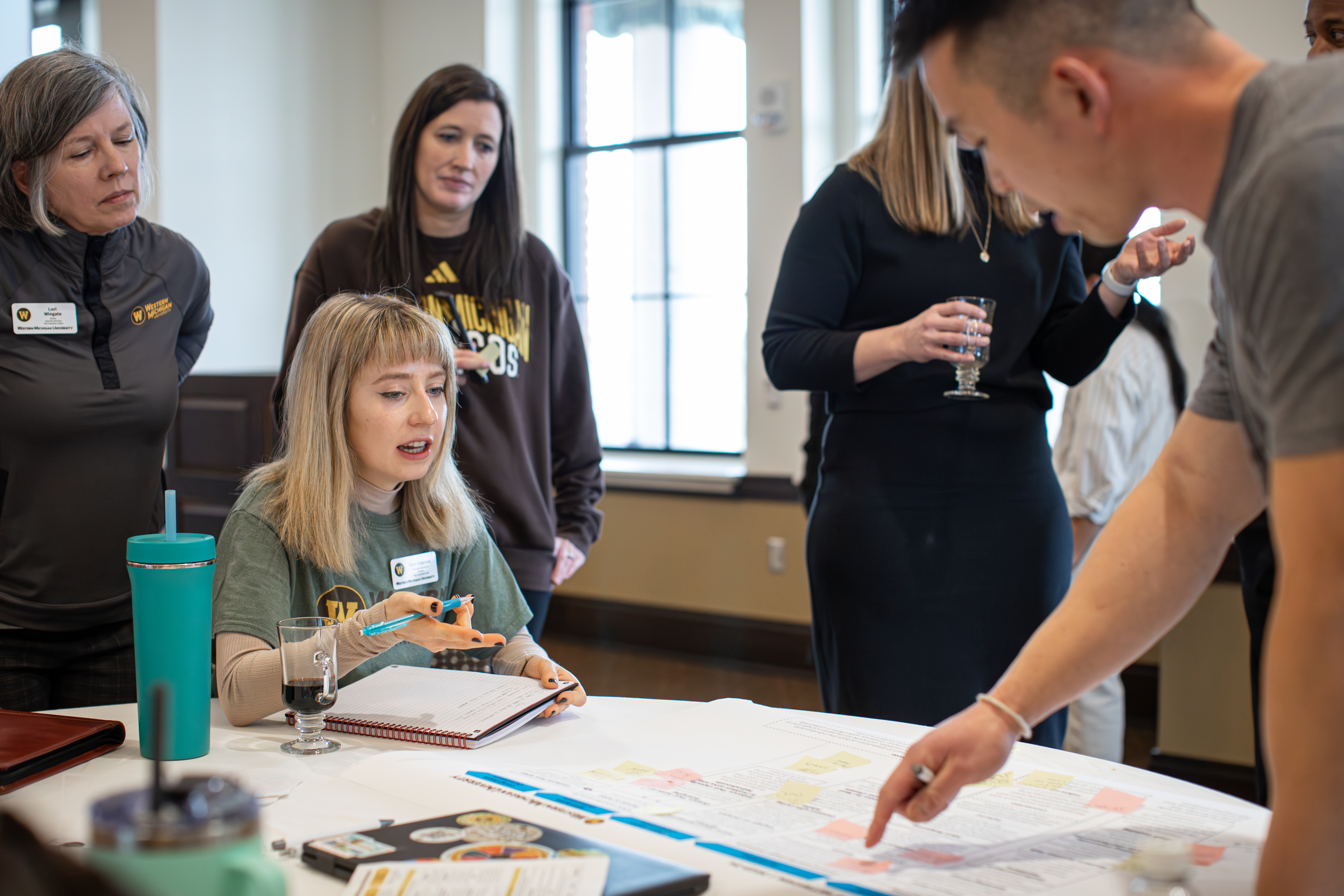 Students and faculty gather around a chart to discuss a plan.