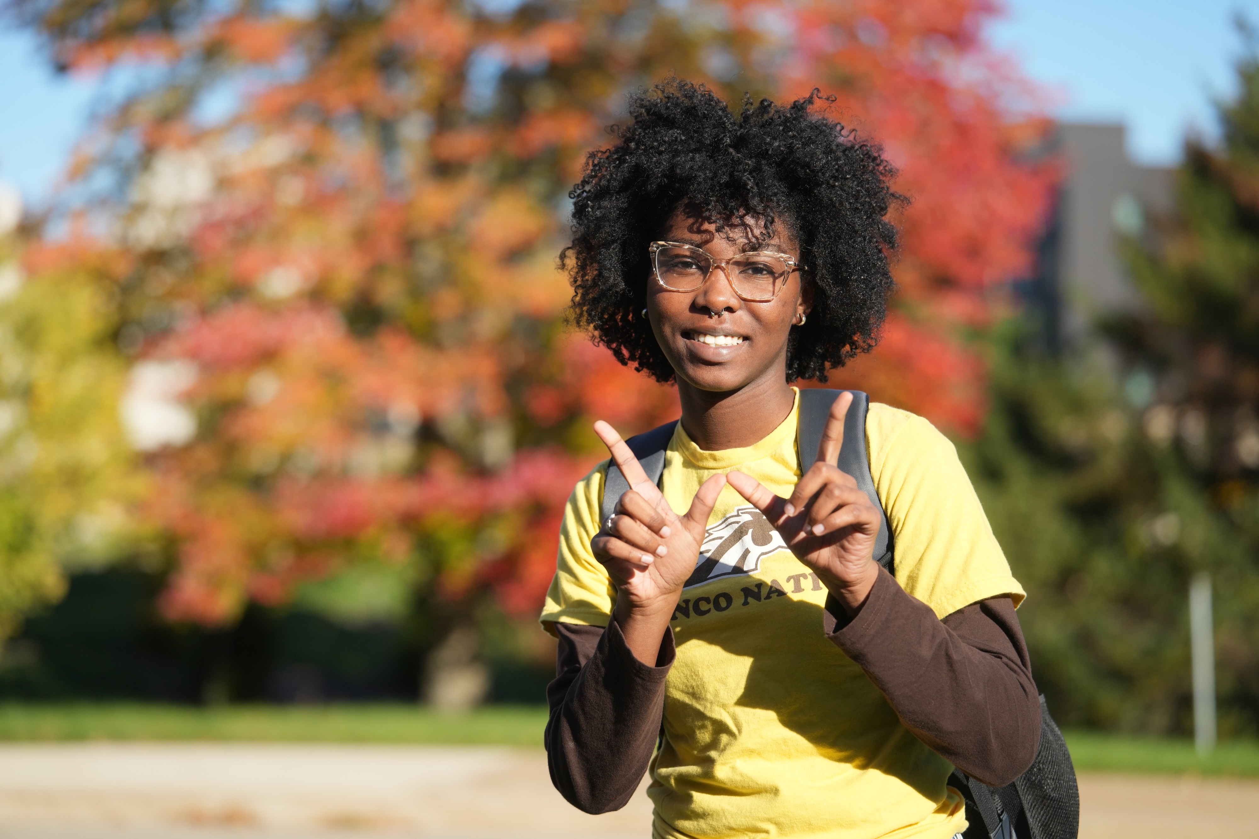 A student in Bronco gear in front of fall leaves.