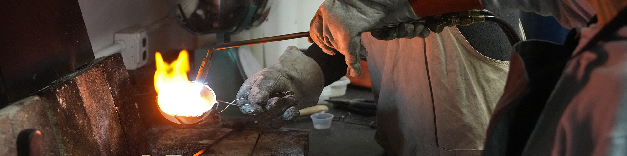 Professor's hands helping a student cast jewelry with a blowtorch.
