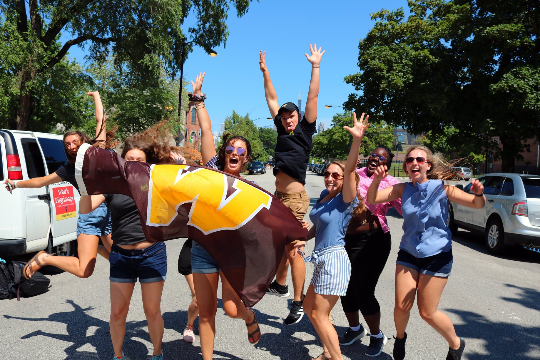 Students holding a WMU flag jumping in happiness. 