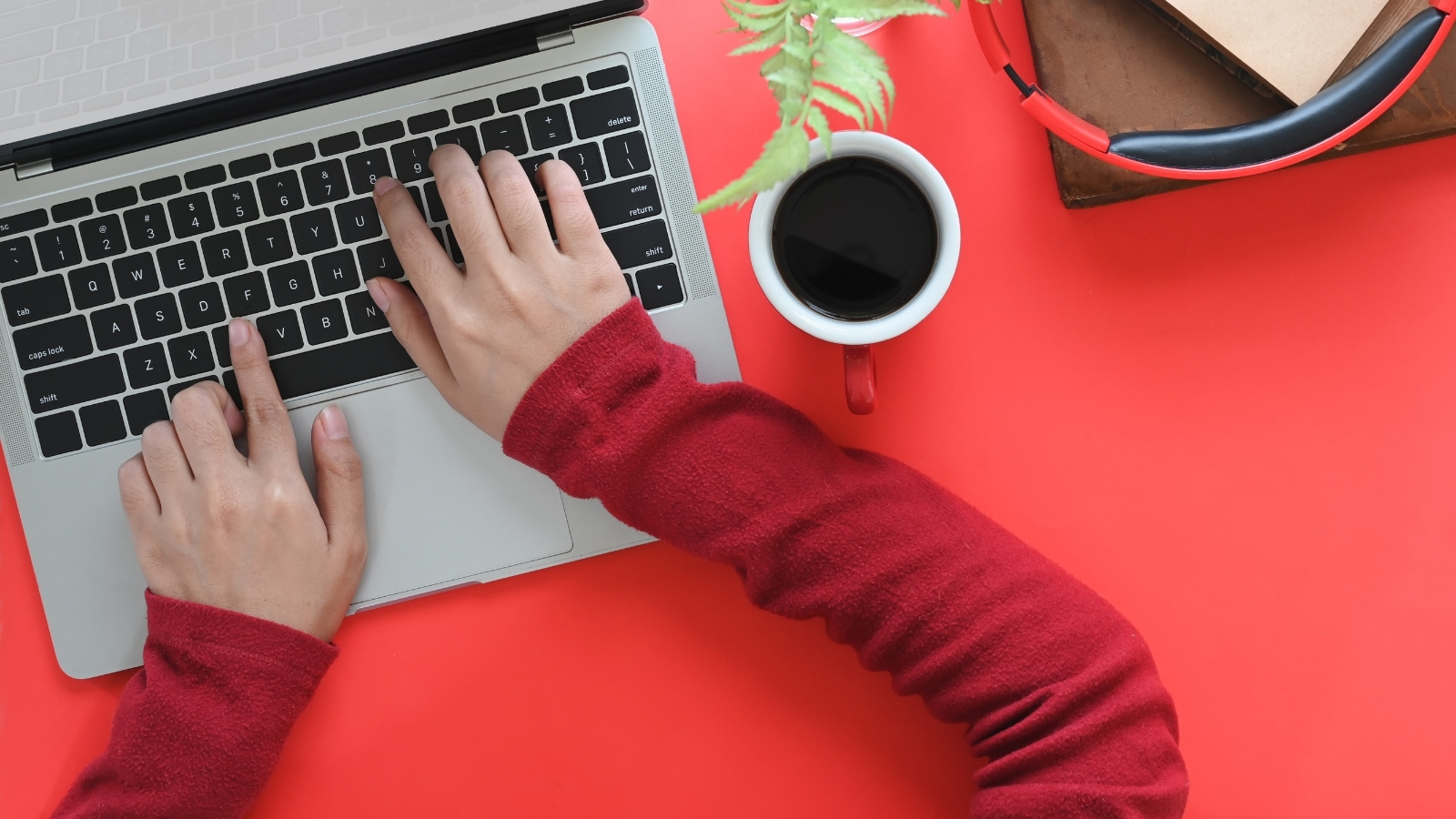 Hands on a laptop with coffee cup and headset nearby.
