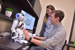 Two students hook up a small robot to a computer.