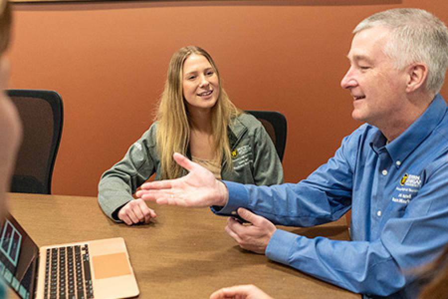 WMU sales program students around a computer with their teacher.