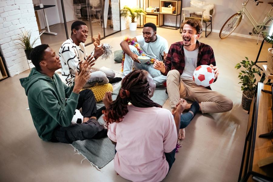 A group diverse men and women sitting in a circle, laughing, hanging out and holding a volleyball.