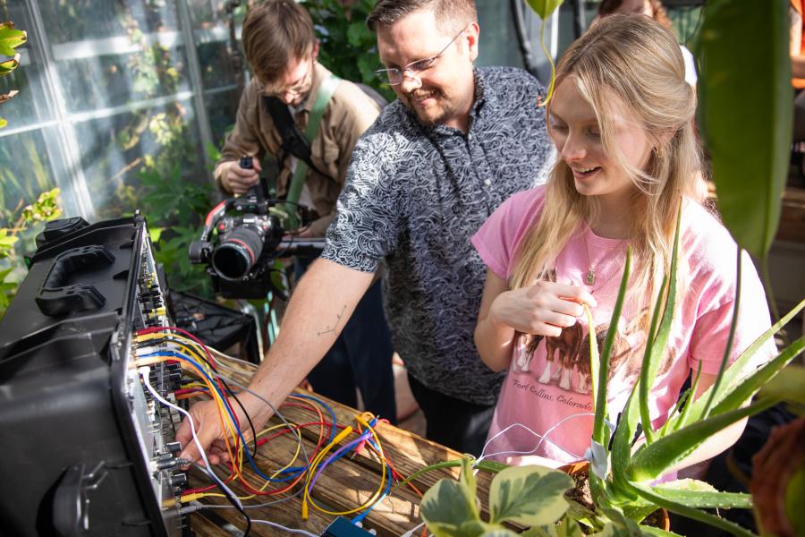 A professor works with a student in a greenhouse next to audio equipment.
