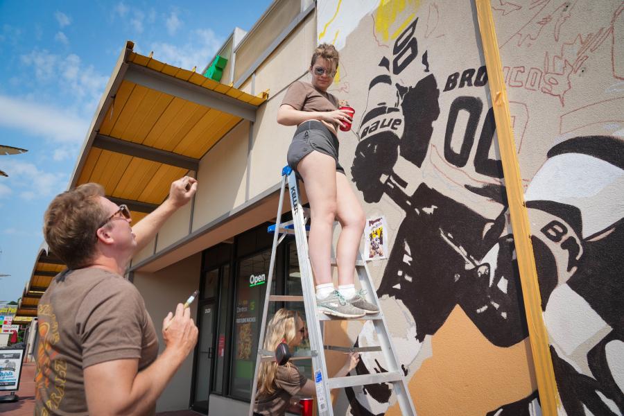 A student stands on a ladder next to a mural.