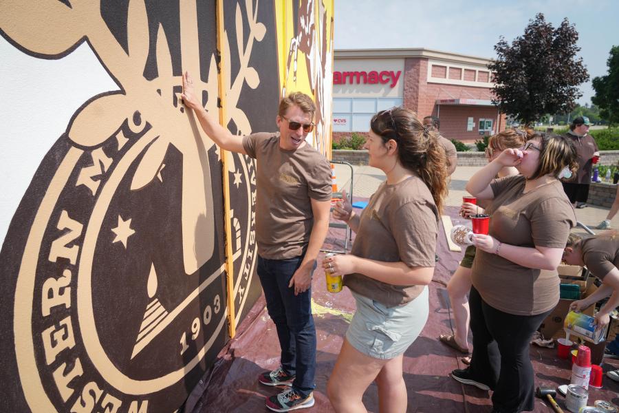 Brad Zenz talks with a student next to a mural.