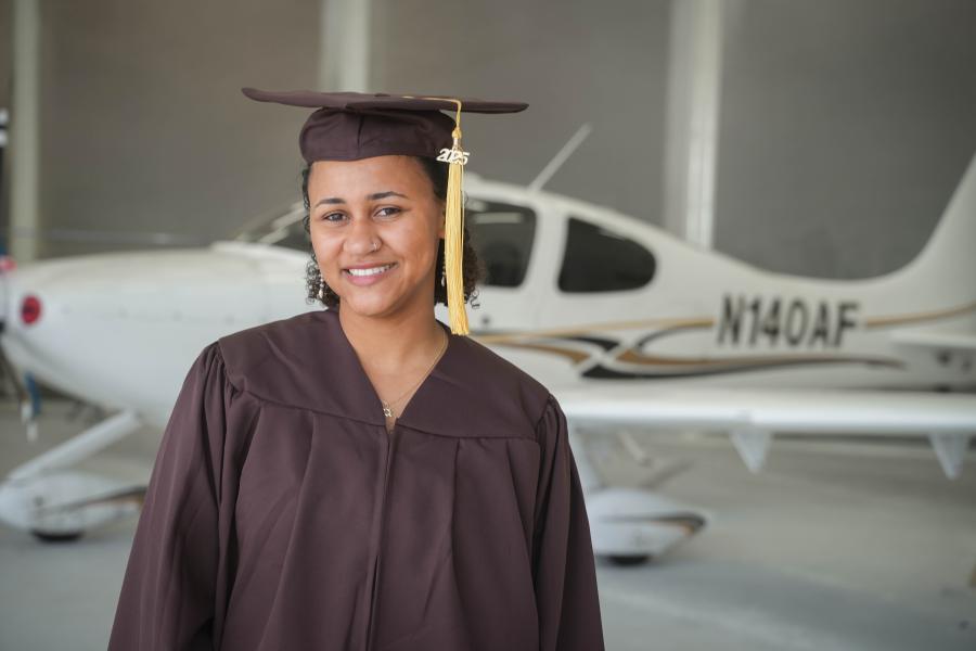 Adaora Osolu wears her graduation cap and gown in front of a plane.