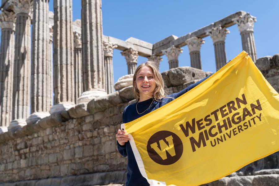 A Bronco holding up a WMU flag in front of the Greek Parthenon.