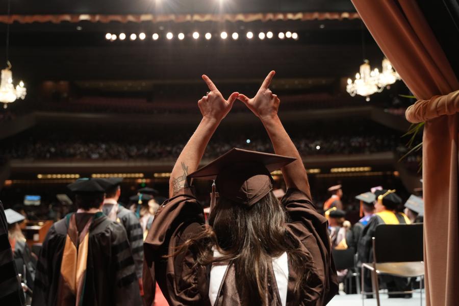 A student creating a W with her hands on the stage of Miller Auditorium at WMU commencement.