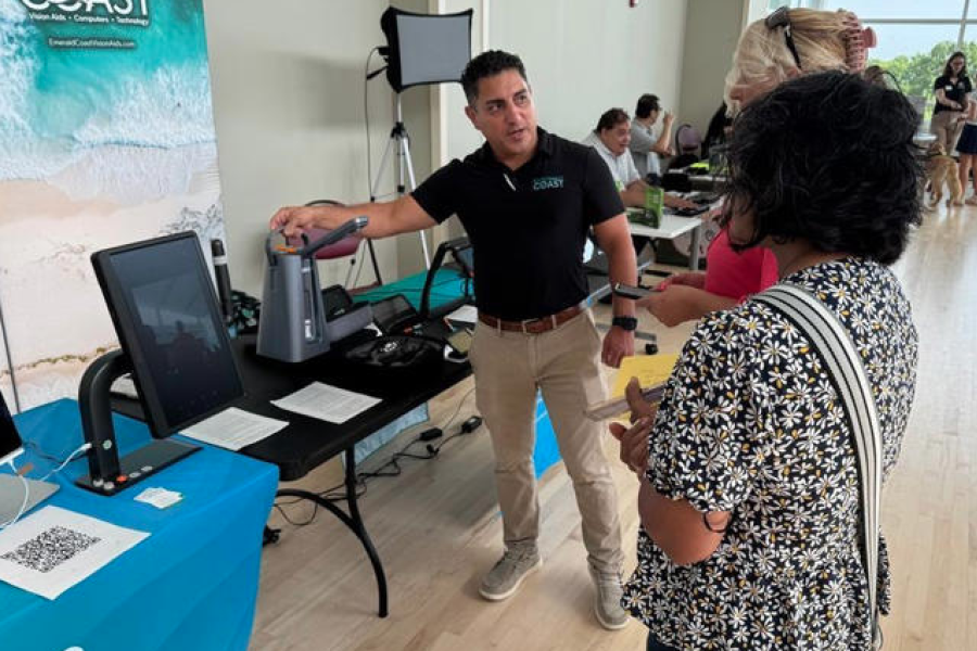 Image of male vendor demonstrating an assistive device for two female onlookers