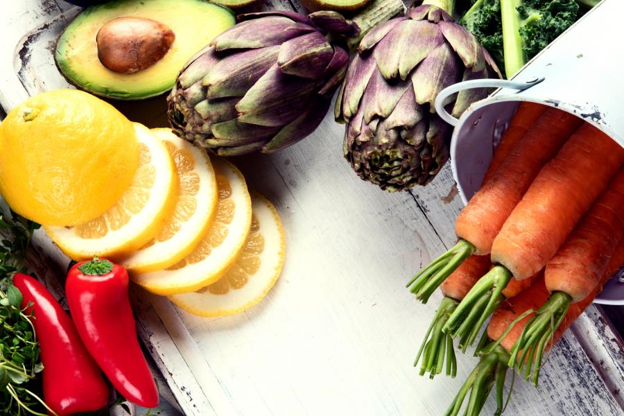 Peppers, sliced lemon, avocado, carrots and artichokes on a white cutting board