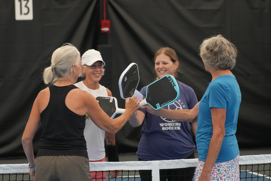 Four ladies at the pickleball net with paddles together.