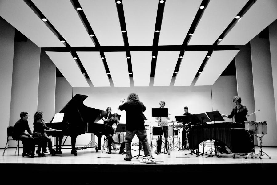 A black and white photo of a mixed-instrumentation chamber ensemble performing on stage.